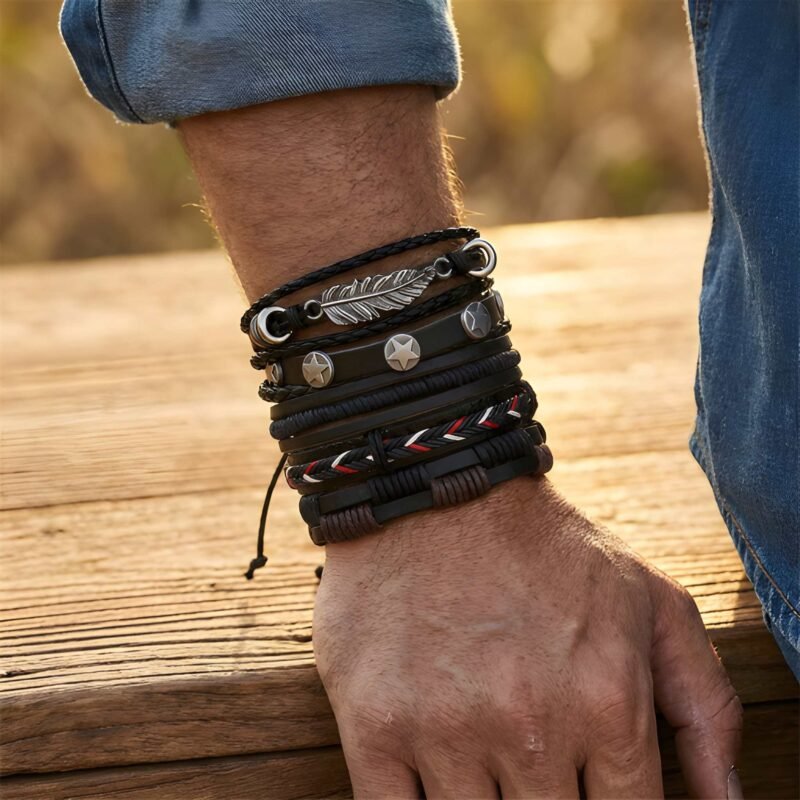Close-up of a man's arm resting on wooden planks outdoors, wearing a stacked black leather bracelet set featuring a silver feather charm and star studs.